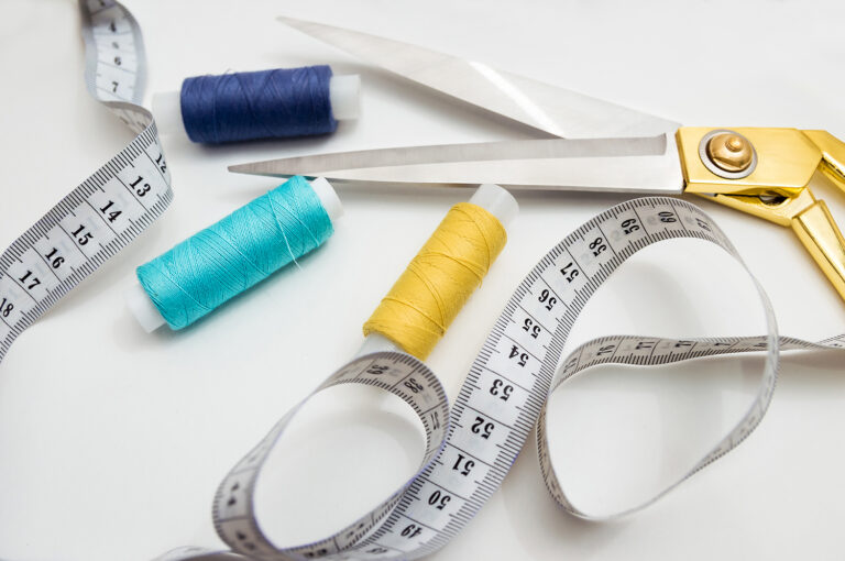golden scissors, blue, blue and yellow threads, measuring tape lying on a white background, a set for cutting and sewing